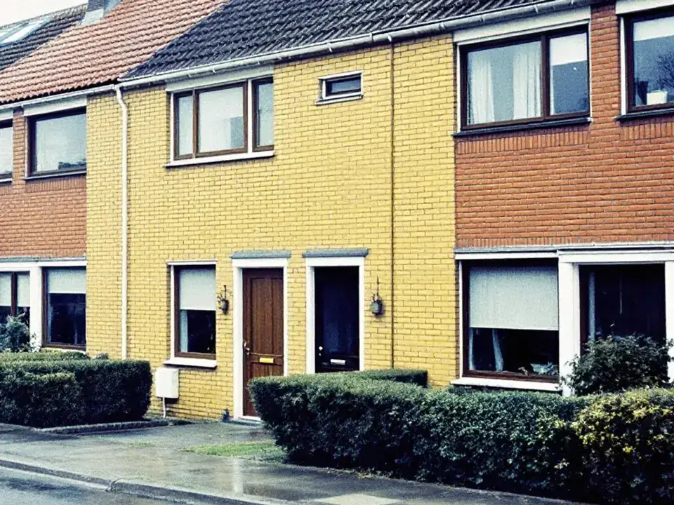 Rijtjeshuizen uit de jaren zeventig met gele en rode baksteen, bruine kozijnen en lage heggen in de voortuin